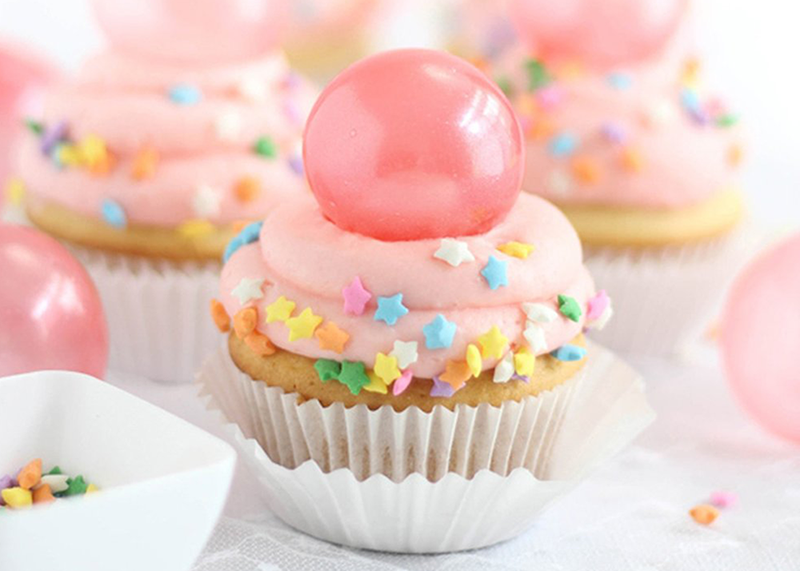 Light cupcake with light pink icing, start-shaped sprinkles, and a large bubble gum sphere on top