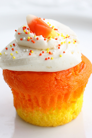 orange and yellow cupcake frosted in white with sprinkles and a piece of candy corn on top