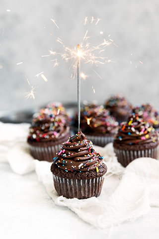 Chocolate cupcakes with chosolate icing. The center cupcake has a lit sparkler in it