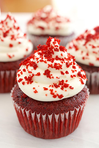 Red cupcake frosted with white frosting and sprinkled with red crumbs